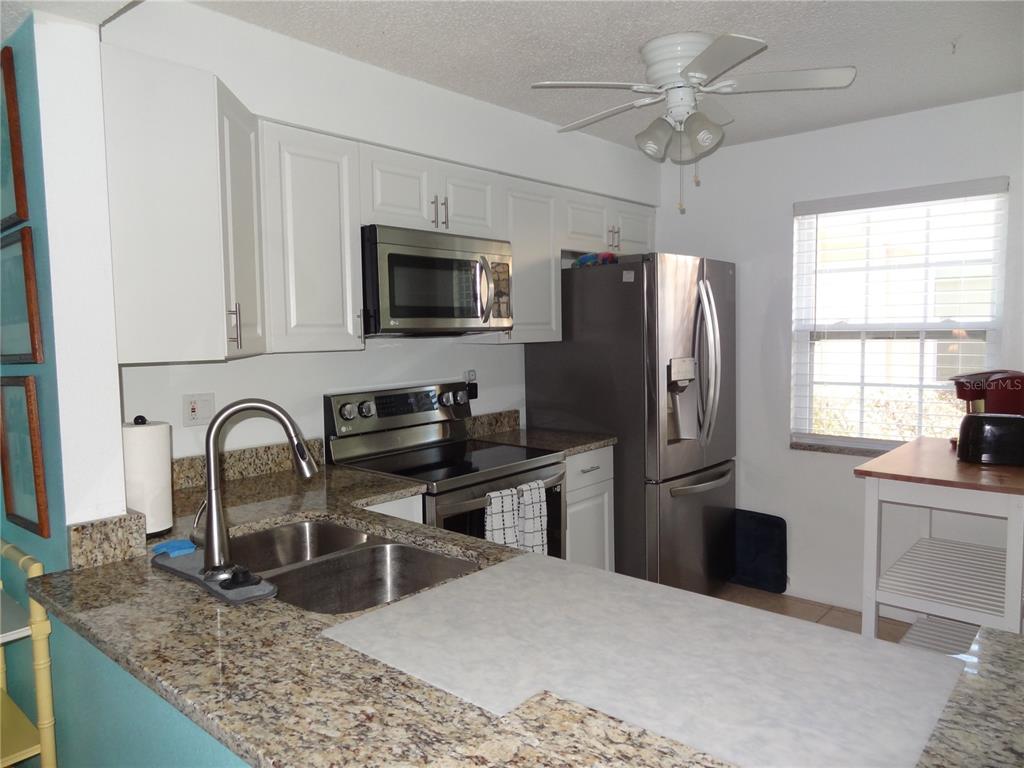 11135 Carriage Hill Drive, Unit 3 Port Richey, FL 34668 - Photo 8 of 25 a kitchen with stainless steel appliances granite countertop a refrigerator a stove a sink a washer and wooden cabinets