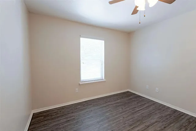 an empty room with wooden floor chandelier fan and windows
