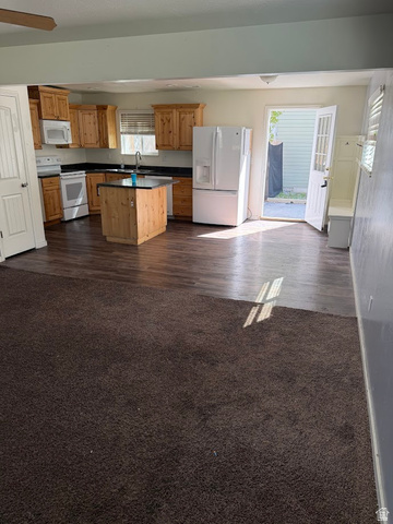 695 West 760 South Logan, UT 84321 - Photo 3 of 5 Kitchen with white appliances, dark countertops, dark carpet, a center island, and wood finish cabinetry