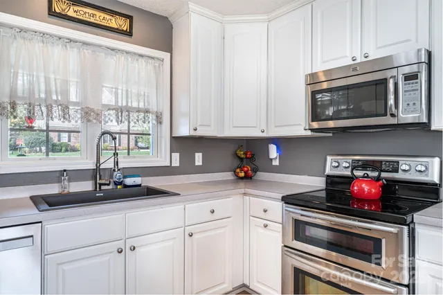 a kitchen with granite countertop white cabinets appliances and a window
