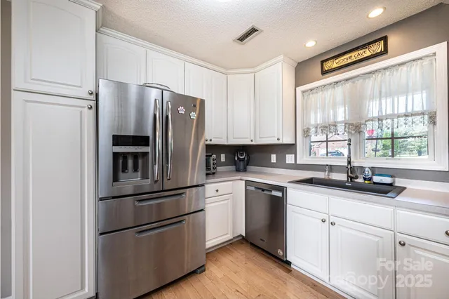 a kitchen with white cabinets white stainless steel appliances and window
