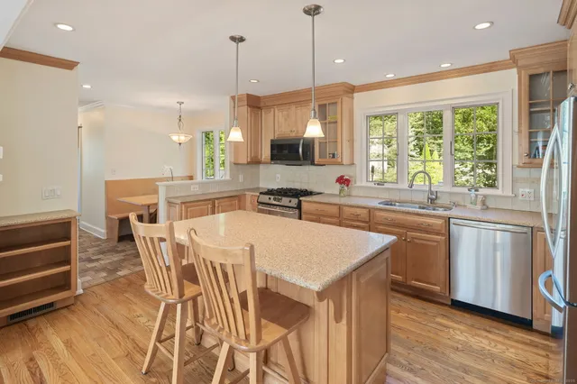 a kitchen with stainless steel appliances granite countertop a stove a sink a microwave a refrigerator a stove a dining table and chairs with wooden floor