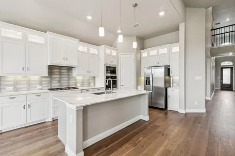 a kitchen with stainless steel appliances granite countertop a refrigerator a sink dishwasher a stove and white countertops with wooden floor