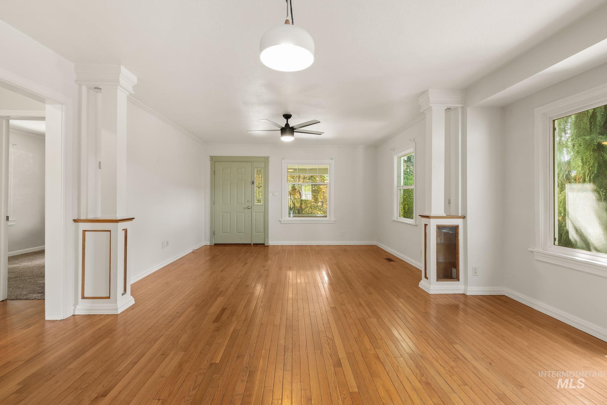 928 3rd Street Clarkston, WA 99403 - Photo 9 of 44 Spacious living area featuring polished wood flooring, abundant natural light from multiple windows, decorative architectural columns, a ceiling fan, and a light-colored entry door with decorative glass