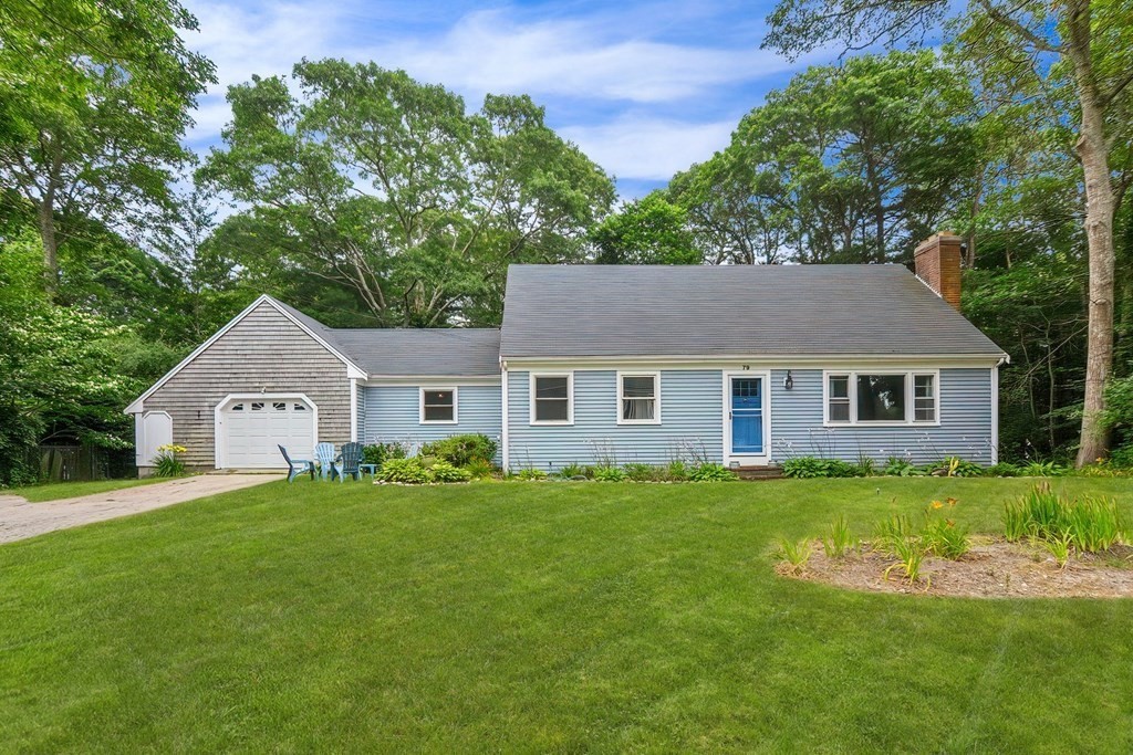 a house that is sitting in the grass with large trees and plants