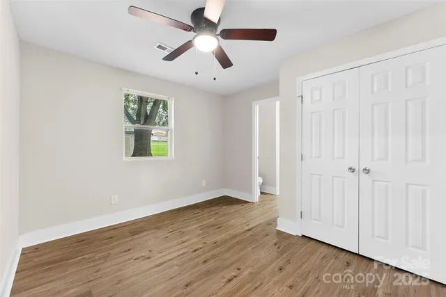 an empty room with wooden floor ceiling fan and windows