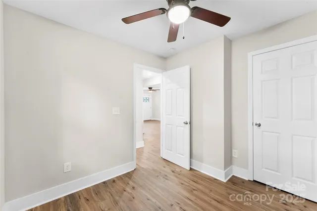 an empty room with wooden floor fan and windows