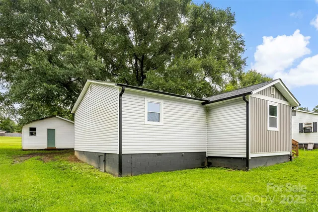 a view of a white house in front of a yard with large tree