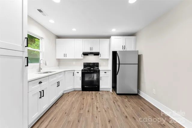 a kitchen with granite countertop a refrigerator oven a sink dishwasher and white cabinets with wooden floor