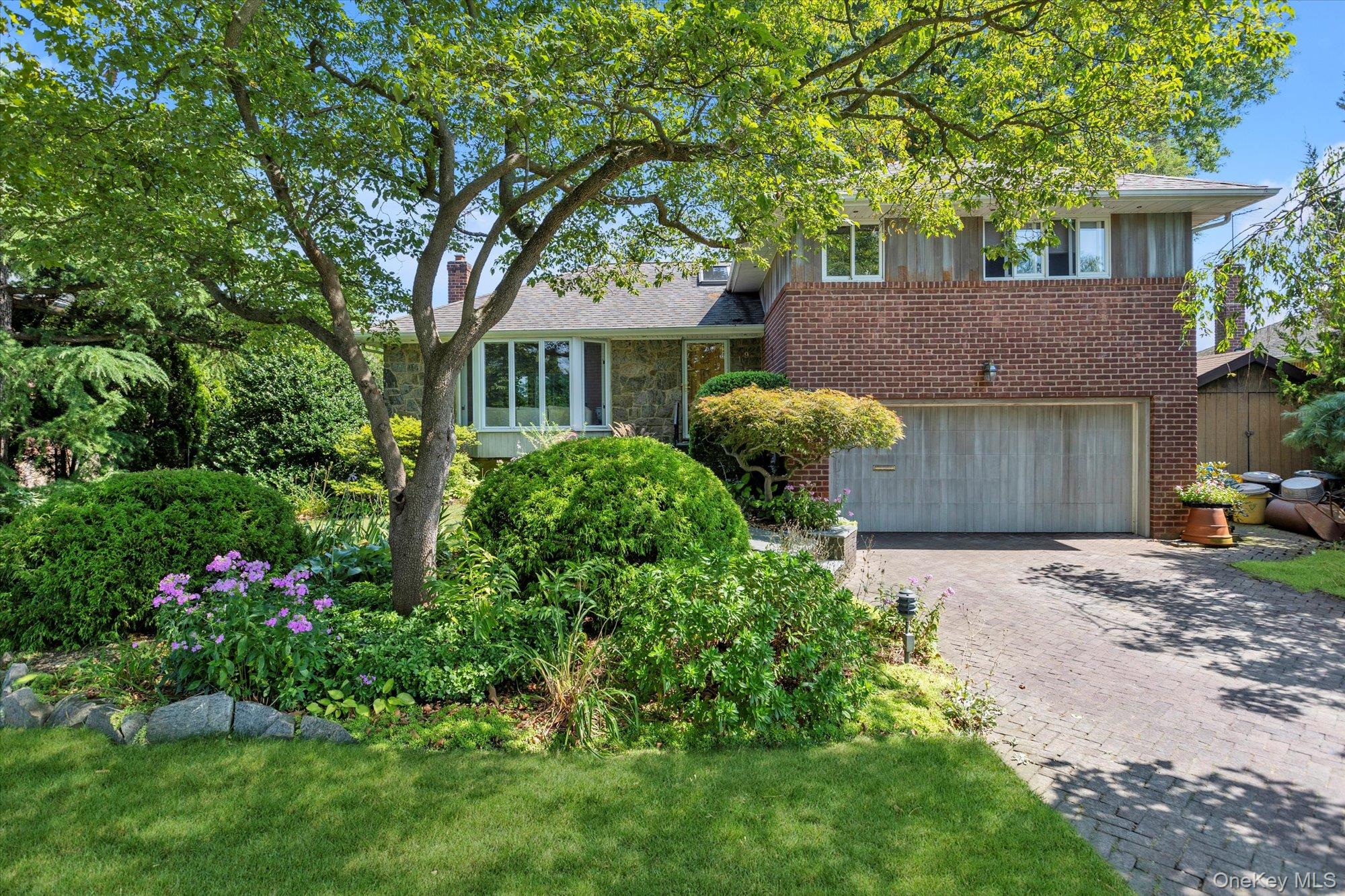 Tri-level home with decorative driveway, a garage, and brick siding