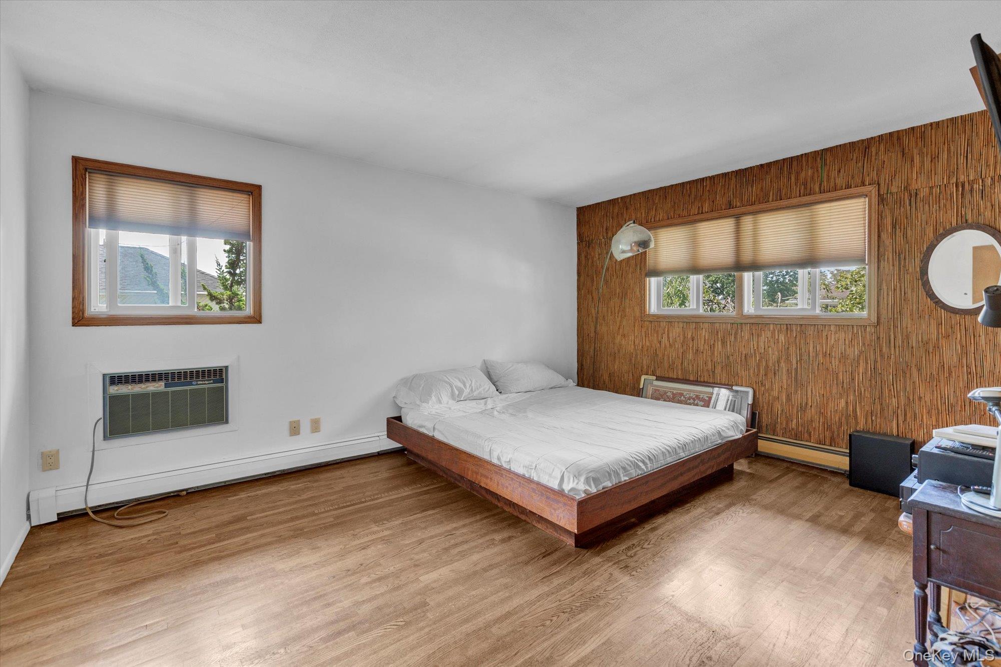 19 Clearland Road Syosset, NY 11791 - Photo 15 of 22 Bedroom with light wood-type flooring, a baseboard heating unit, wood walls, and a wall unit AC