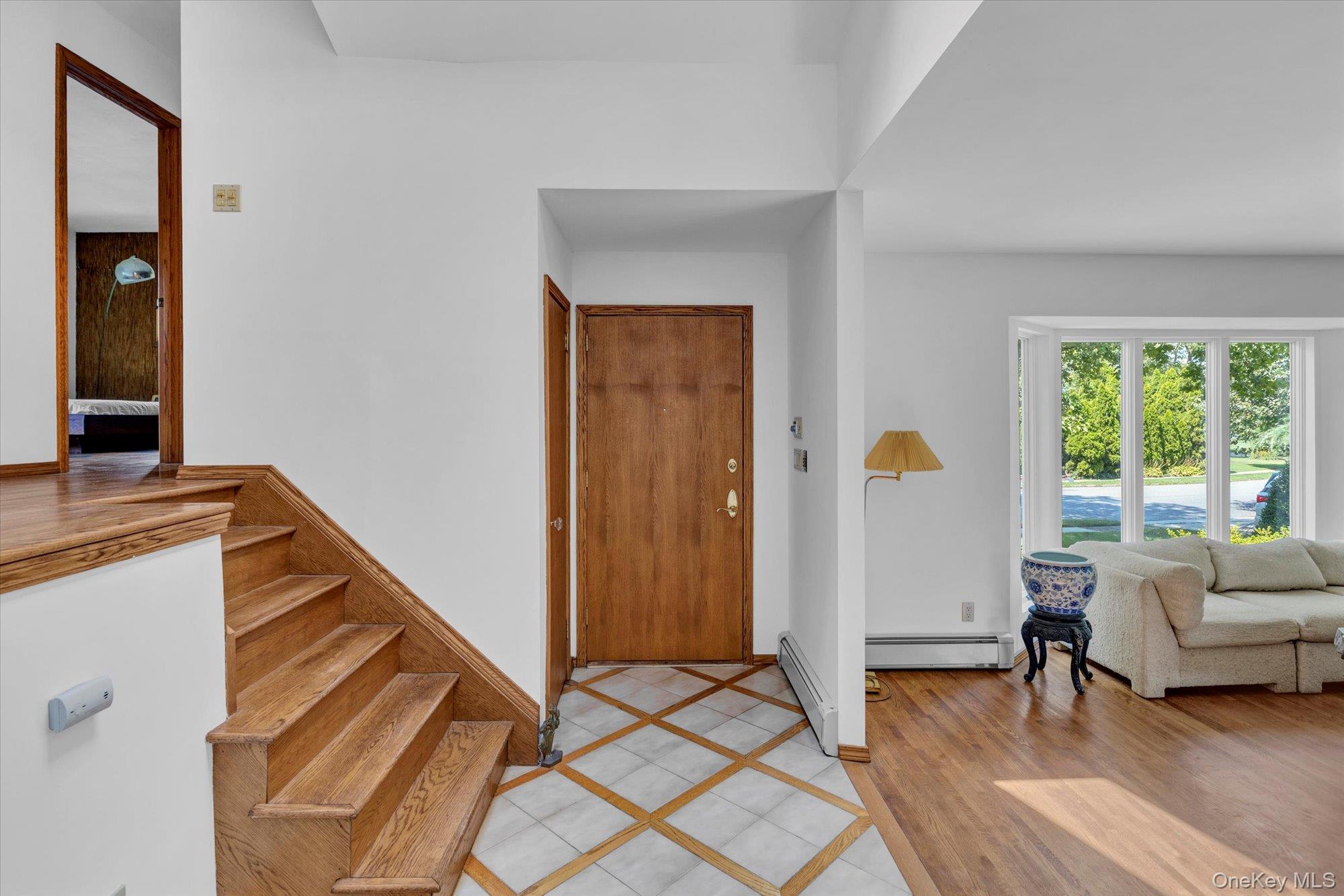19 Clearland Road Syosset, NY 11791 - Photo 4 of 22 Foyer entrance featuring inlaid floor details, a baseboard radiator, stairway, and light wood-style flooring