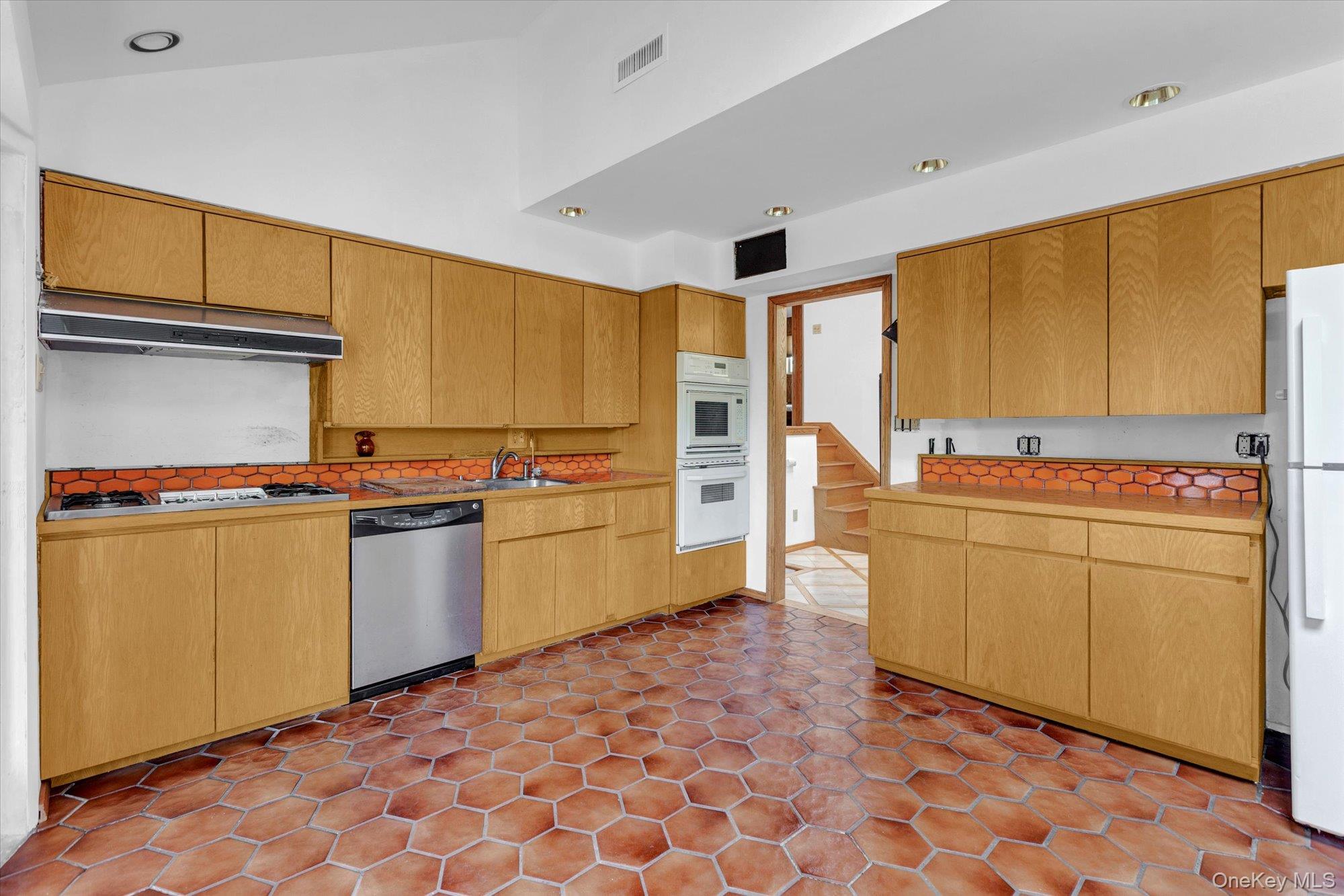 19 Clearland Road Syosset, NY 11791 - Photo 9 of 22 Kitchen with white appliances, light countertops, vaulted ceiling, under cabinet range hood, and backsplash