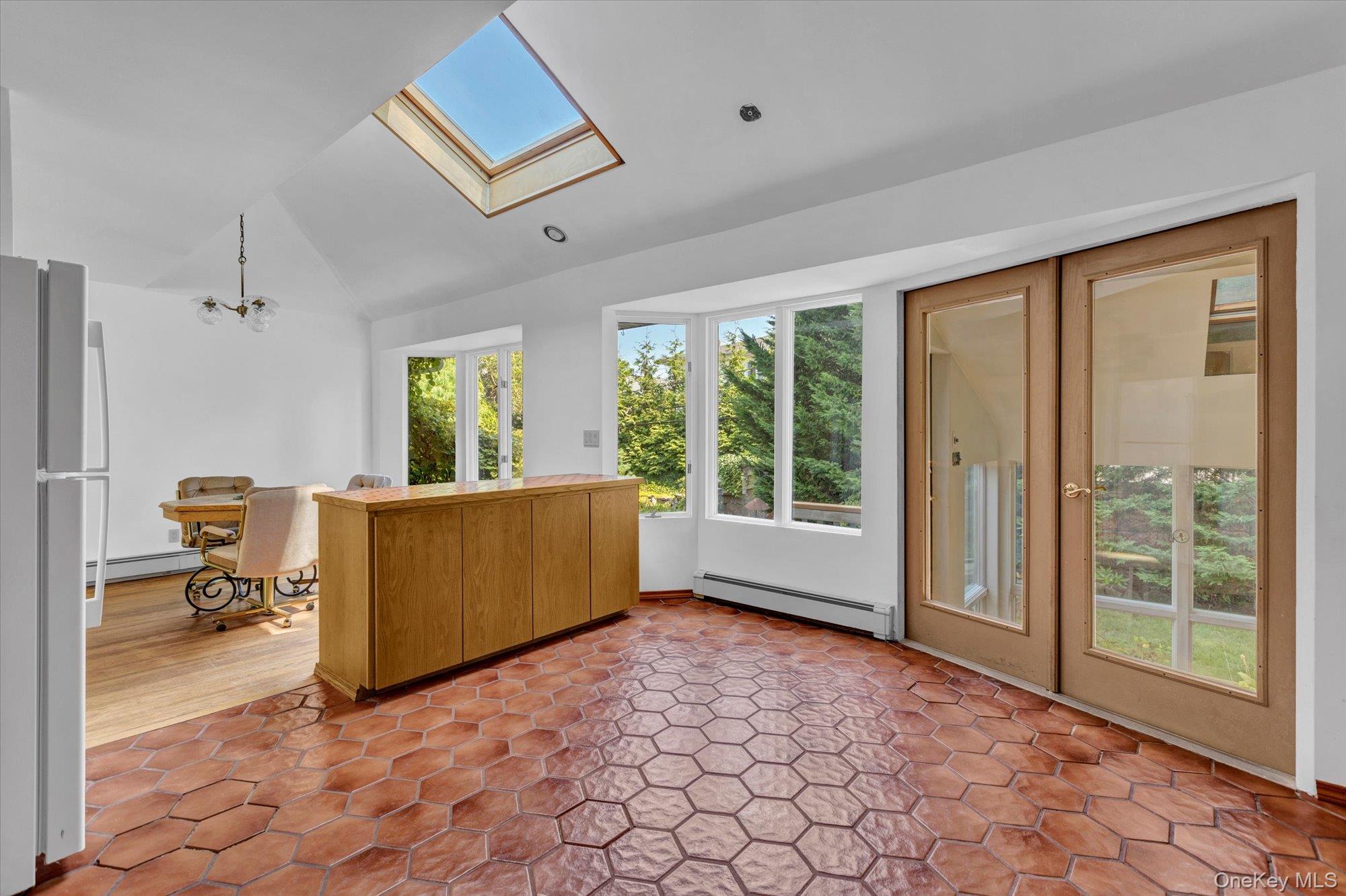 19 Clearland Road Syosset, NY 11791 - Photo 10 of 22 Kitchen featuring vaulted ceiling, freestanding refrigerator, a chandelier, baseboard heating, and a skylight