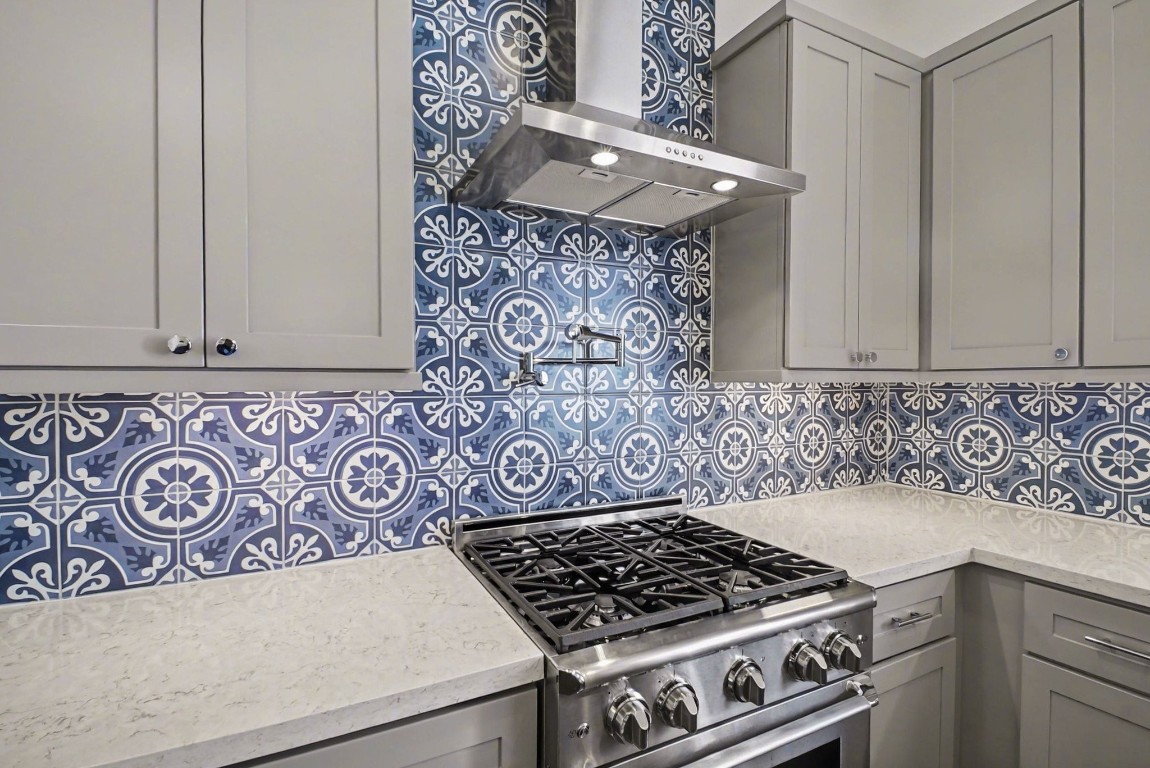 3507 Ridgeway Valley Lane Houston, TX 77055 - Photo 7 of 50 This kitchen features stylish blue and white patterned tile backsplash, complemented by sleek gray cabinets and a modern stainless steel gas stove with a range hood and pot filler. The light countertops enhance the bright, contemporary feel.