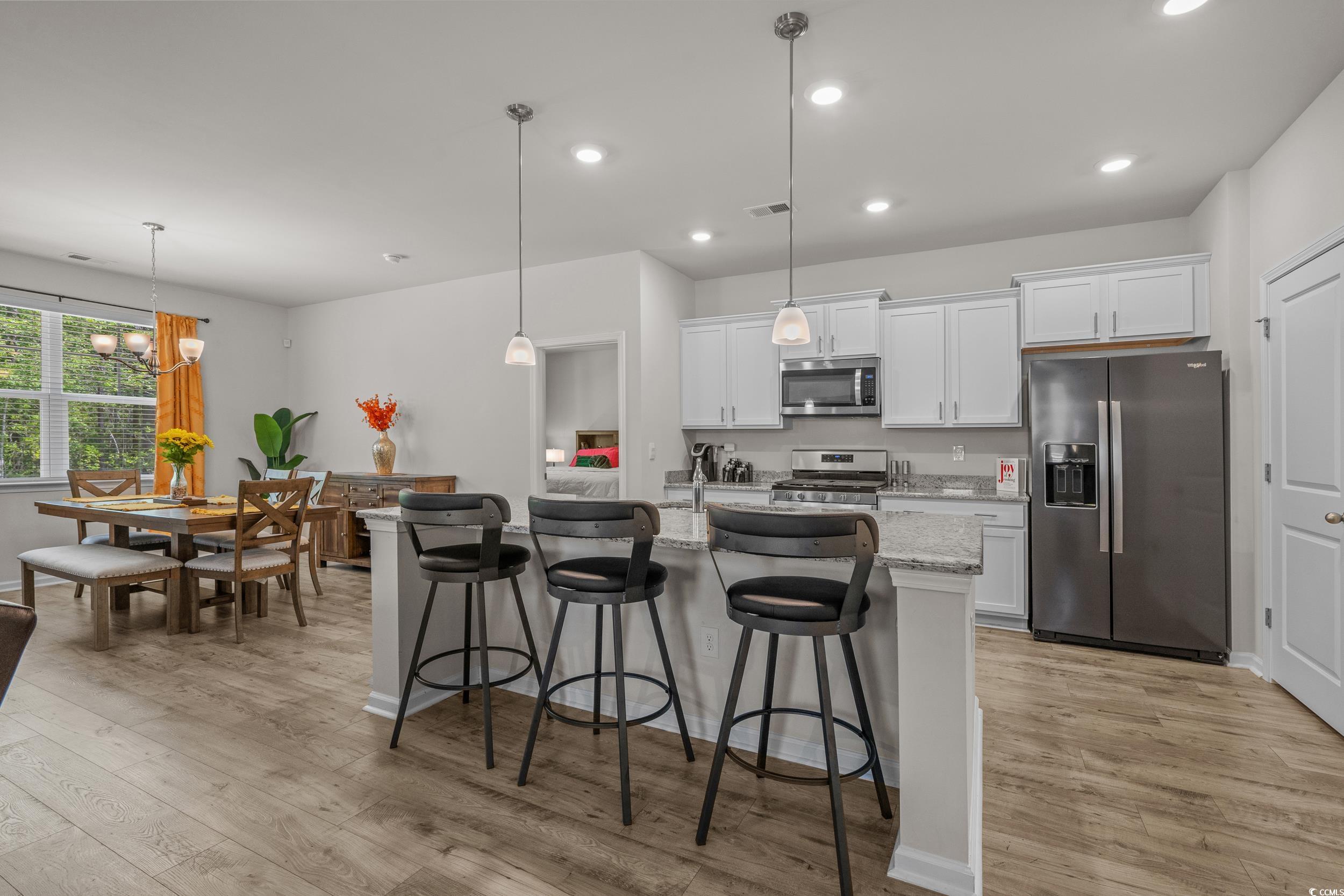 847 Flowering Br Avenue Little River, SC 29566 - Photo 9 of 30 Kitchen featuring stainless steel appliances, pendant lighting, white cabinetry, a kitchen bar, and light stone countertops