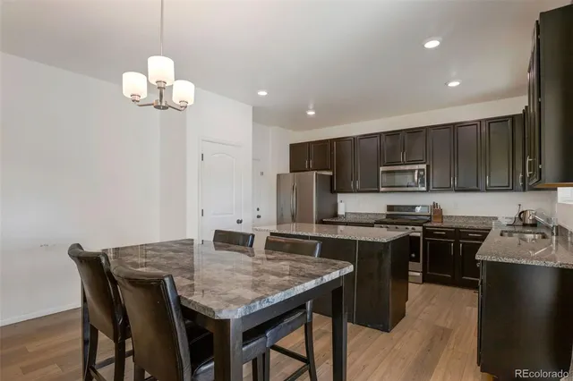 a kitchen with stainless steel appliances granite countertop a stove top oven a refrigerator a sink a dining table and chairs