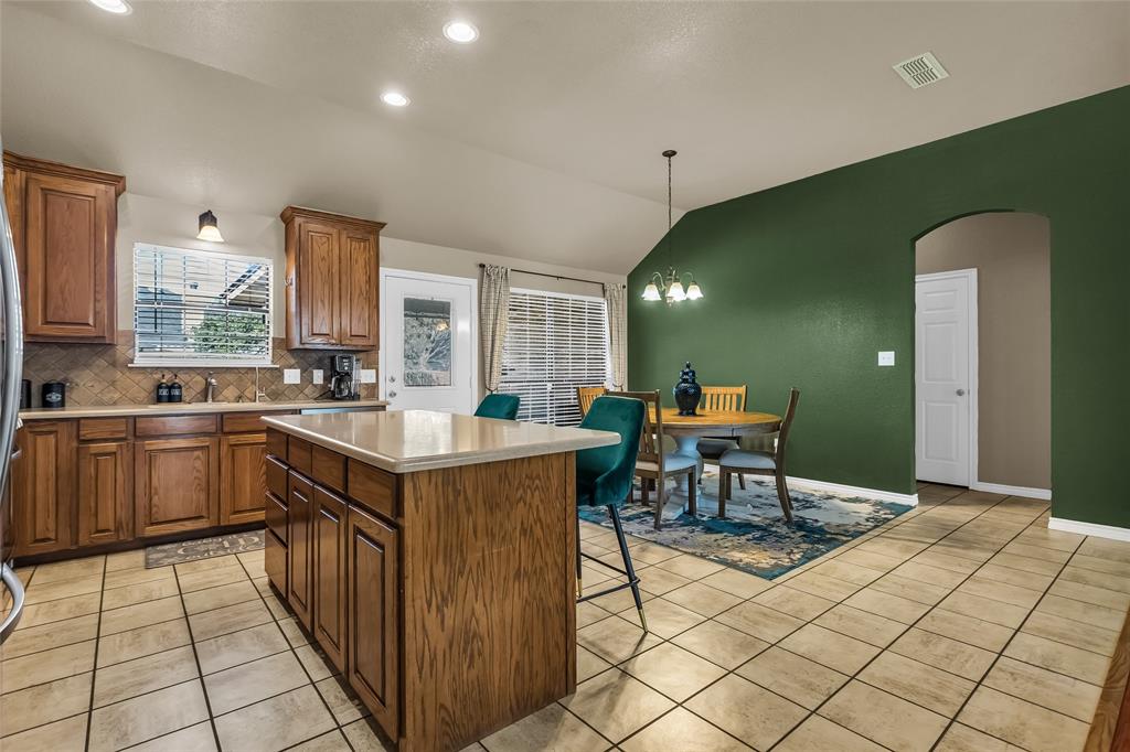 226 King George Road Ponder, TX 76259 - Photo 25 of 39 Kitchen featuring vaulted ceiling, brown cabinets, a center island, backsplash, and light tile patterned floors