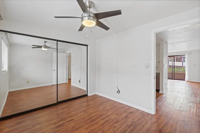 an empty room with wooden floor fan and windows