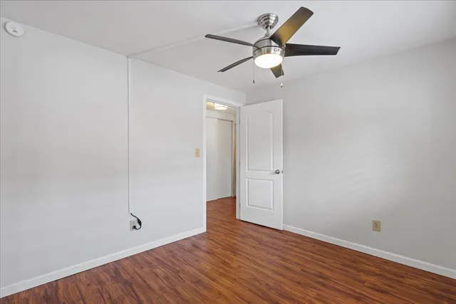 an empty room with wooden floor fan and windows