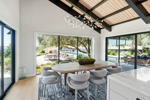 a view of a dining room with furniture a chandelier and large windows