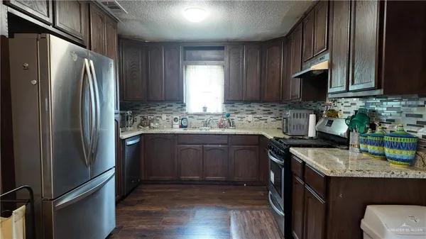 a kitchen with stainless steel appliances granite countertop a refrigerator a sink a stove and wooden cabinets