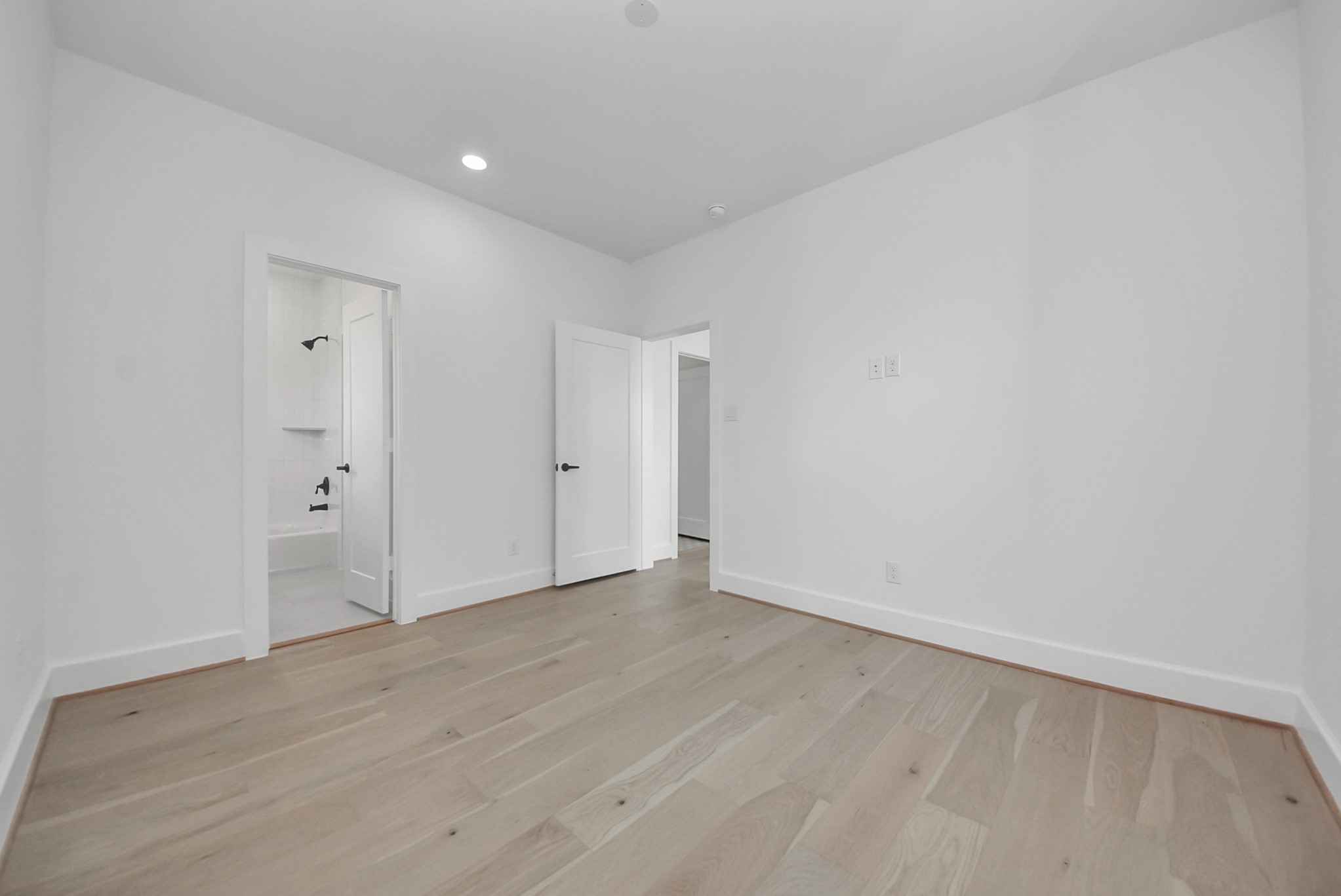 927 Fisher Street, Unit B Houston, TX 77018 - Photo 31 of 47 A clean, bright room with light wood flooring, white walls, and recessed lighting features two doors, one leading to a bathroom. The space’s modern, neutral design provides a versatile layout ready for personal touches.
