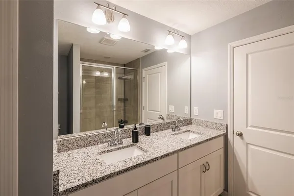 a bathroom with a granite countertop double vanity sink and mirror