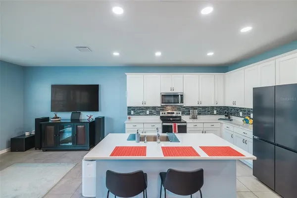 a room with kitchen island stainless steel appliances a stove sink refrigerator and microwave