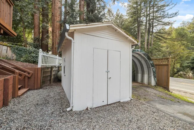 a view of a grey house with large trees and a small barn