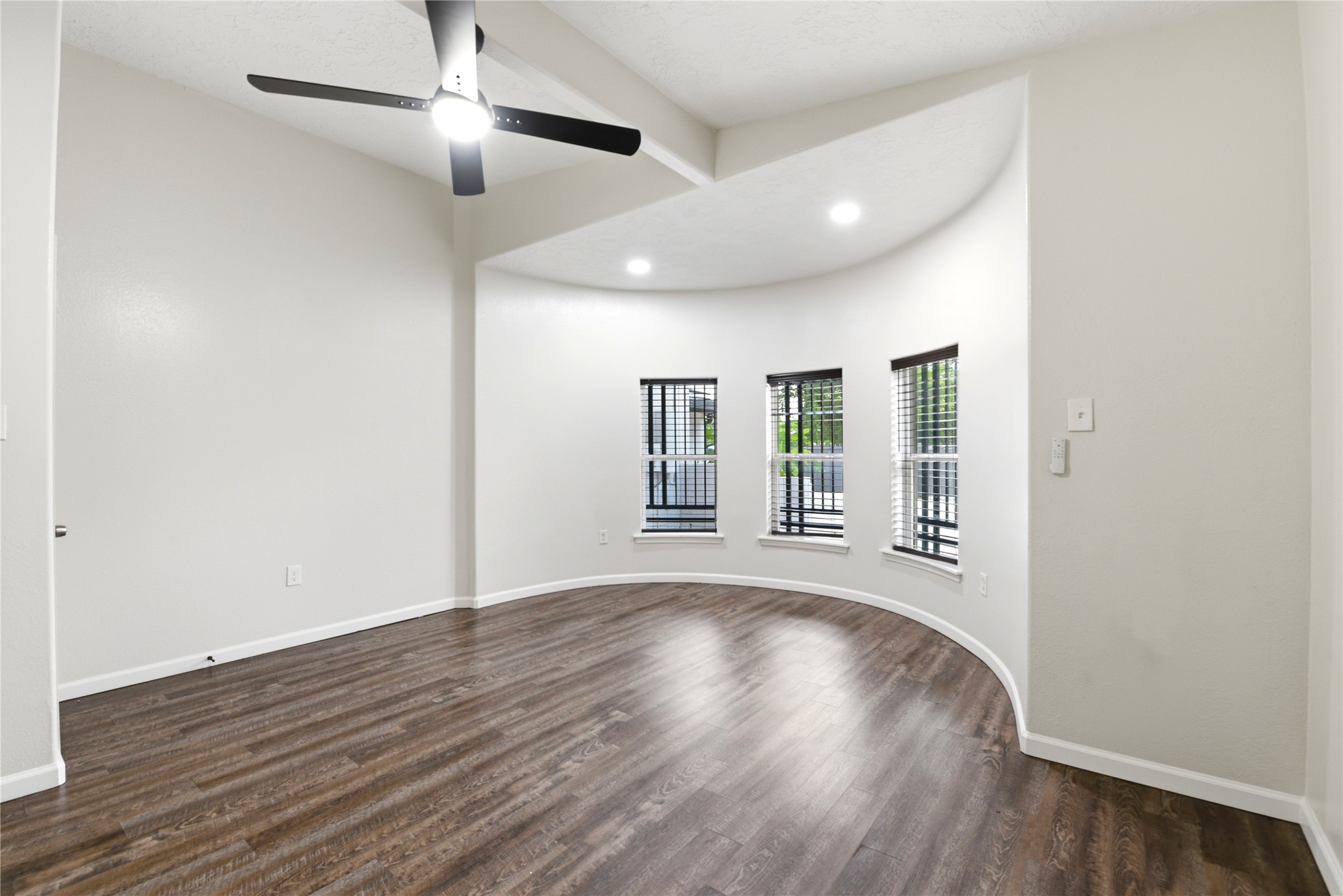 9403 Spaulding Street Houston, TX 77016 - Photo 18 of 50 This photo showcases a bright, open room with a curved wall of three large windows, allowing plenty of natural light. The space features elegant wood flooring, neutral walls, and a modern ceiling fan, perfect for a cozy sitting area or home office.