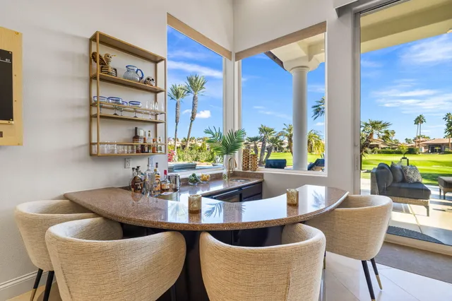 a kitchen with stainless steel appliances granite countertop a stove a sink a refrigerator white cabinets and chairs with wooden floor