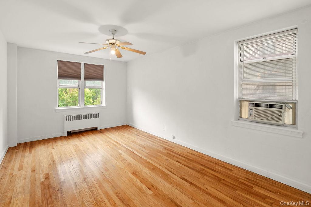 485 Bronx River Road, Unit A21 Yonkers, NY 10704 - Photo 10 of 18 an empty room with wooden floor chandelier fan and windows