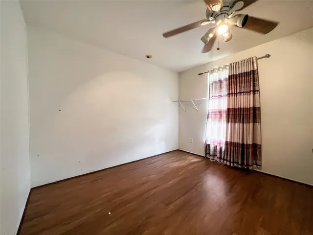 an empty room with wooden floor fan and windows