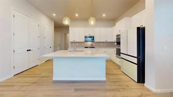 a large kitchen with kitchen island a sink a stove a refrigerator and white cabinets with wooden floor