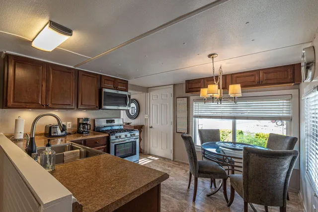 a kitchen with stainless steel appliances granite countertop a stove a refrigerator a sink a dining table and chairs with wooden floor