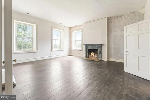 an empty room with wooden floor fireplace and windows