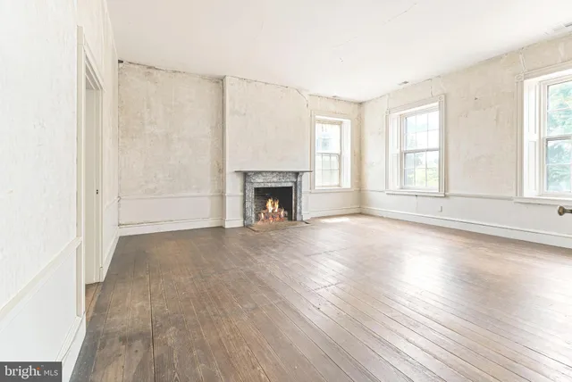 an empty room with wooden floor fireplace and windows