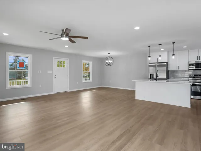 a view of an empty room with kitchen and window