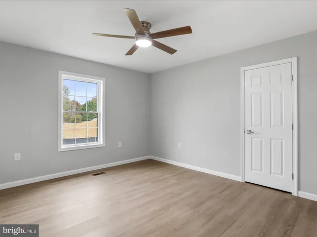 an empty room with wooden floor ceiling fan and windows