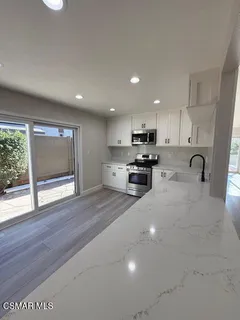 a kitchen with stainless steel appliances granite countertop a stove a sink a refrigerator with white cabinets and wooden floor