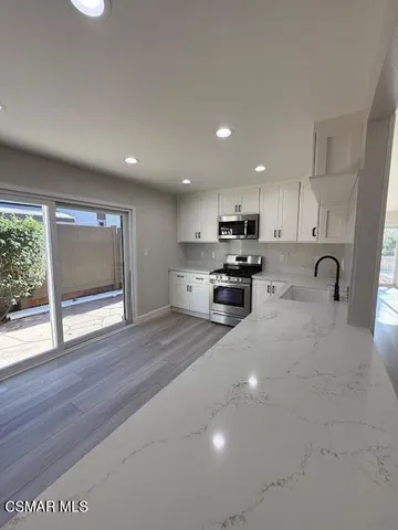 a kitchen with stainless steel appliances granite countertop a stove a sink a refrigerator with white cabinets and wooden floor