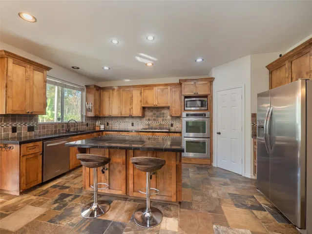 a kitchen with stainless steel appliances granite countertop a refrigerator a sink a stove a dining table and chairs