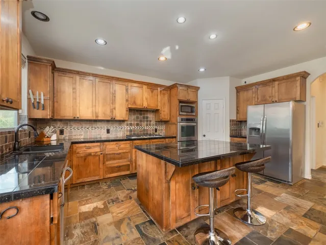 a kitchen with stainless steel appliances granite countertop a sink a stove a refrigerator cabinets and chairs