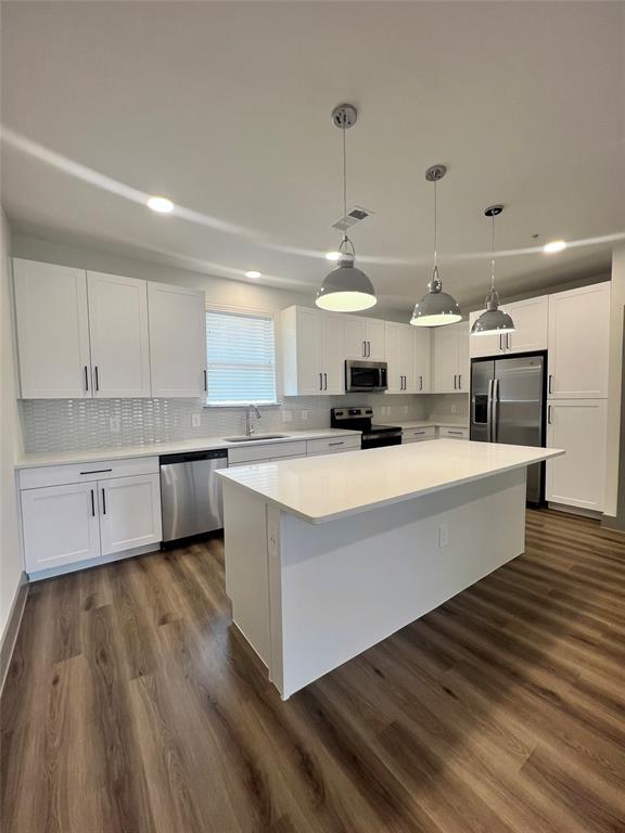 a large white kitchen with kitchen island a stove a sink dishwasher and white cabinets with wooden floor