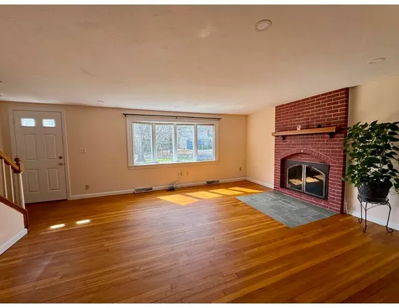 an empty room with wooden floor fireplace and windows