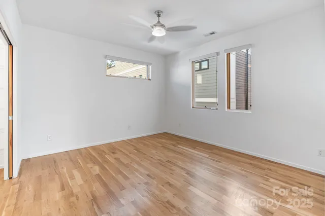 an empty room with wooden floor ceiling fan and windows