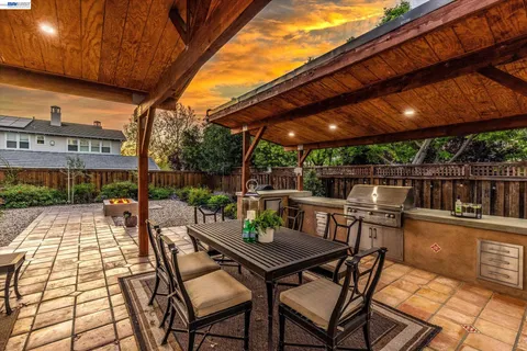 a view of a patio with table and chairs under an umbrella with a barbeque