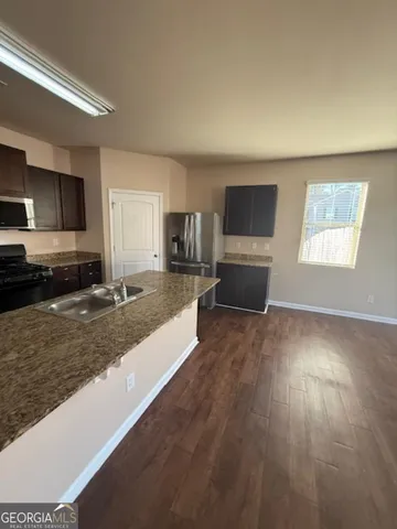 a large kitchen with kitchen island granite countertop a stove a sink a refrigerator white cabinets and wooden floor