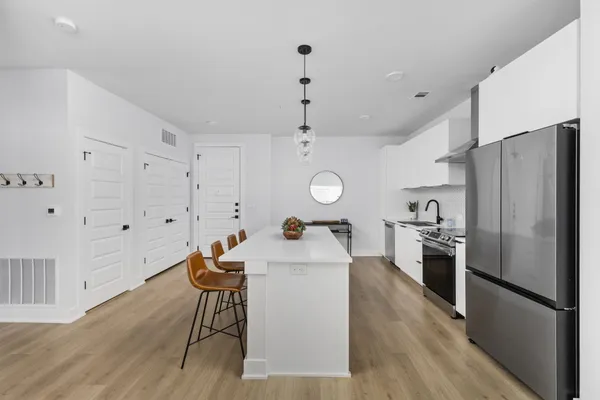 a kitchen with stainless steel appliances granite countertop a refrigerator a sink dishwasher a dining table and chairs with wooden floor